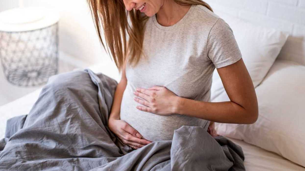 Photo of happy mid adult pregnant woman relaxing at home and looking at her future baby.