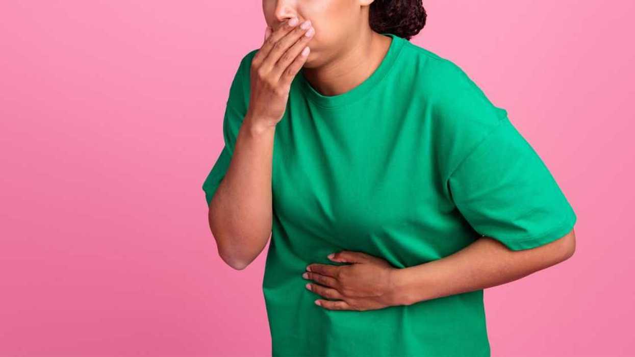 Photo portrait of a pretty young girl as she covers her mouth. She suffera nausea and wears a trendy green outfit isolated on a pink color background.