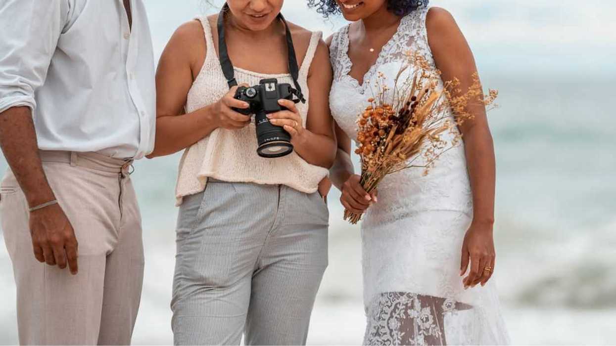 Photographer shows wedding photos to the bride and groom, on the beach.