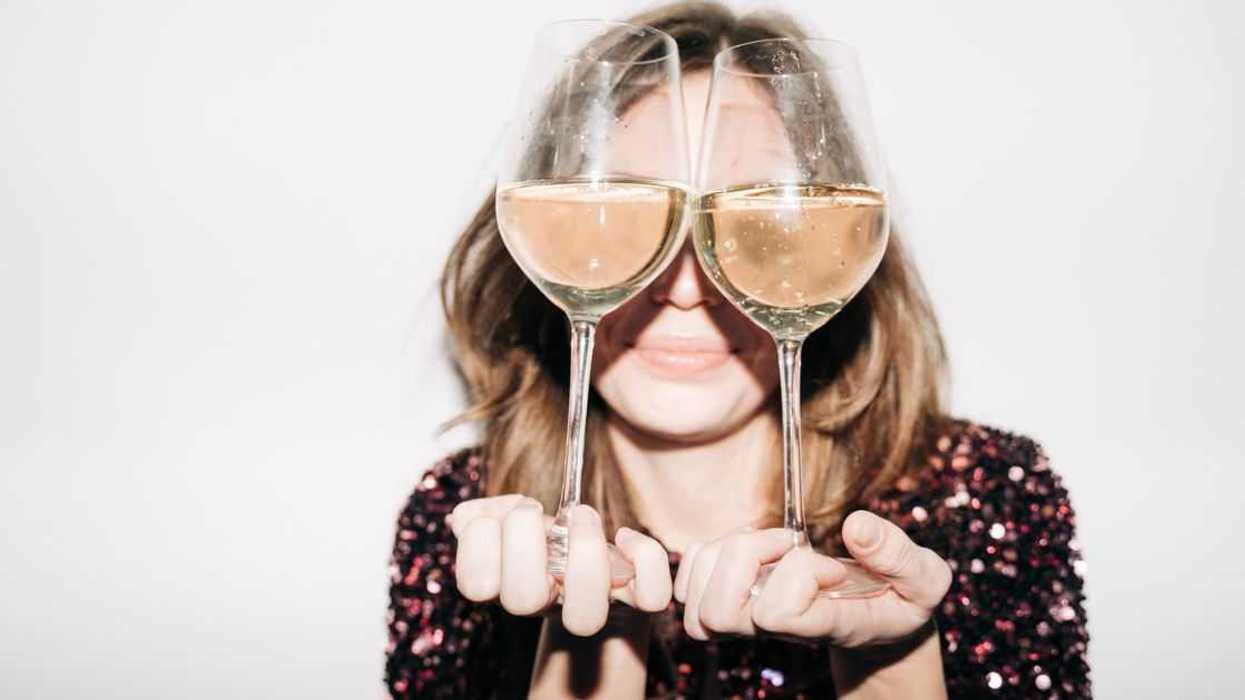 Portrait if a young, blonde woman holding two large glasses of champagne in front of her eyes.