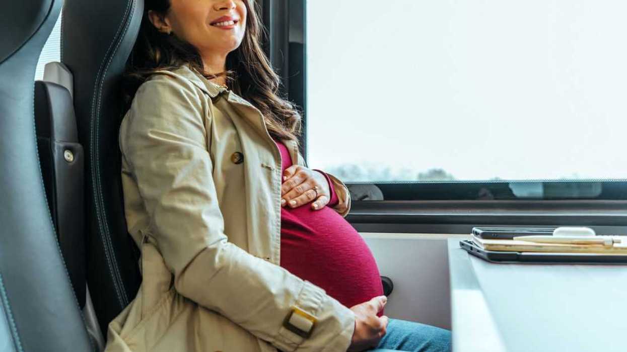 Portrait of a beautiful young expectant mother touching her belly while commuting on a train.