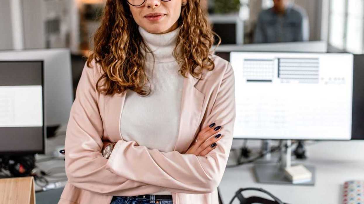 Portrait of a business woman standing in the office with arms crossed, looking at camera, smiling.