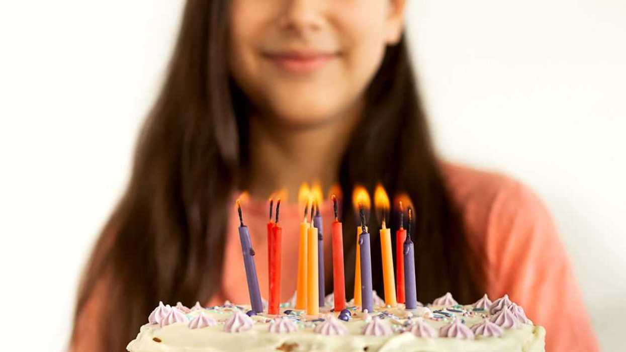 Portrait of joyful teen girl blowing candles on abirthday cake. White wall background.