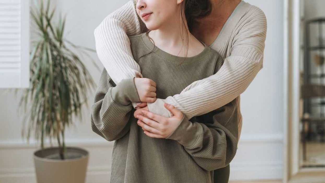 Portrait of middle age woman, a mother and a teenager daughter together in light interior.