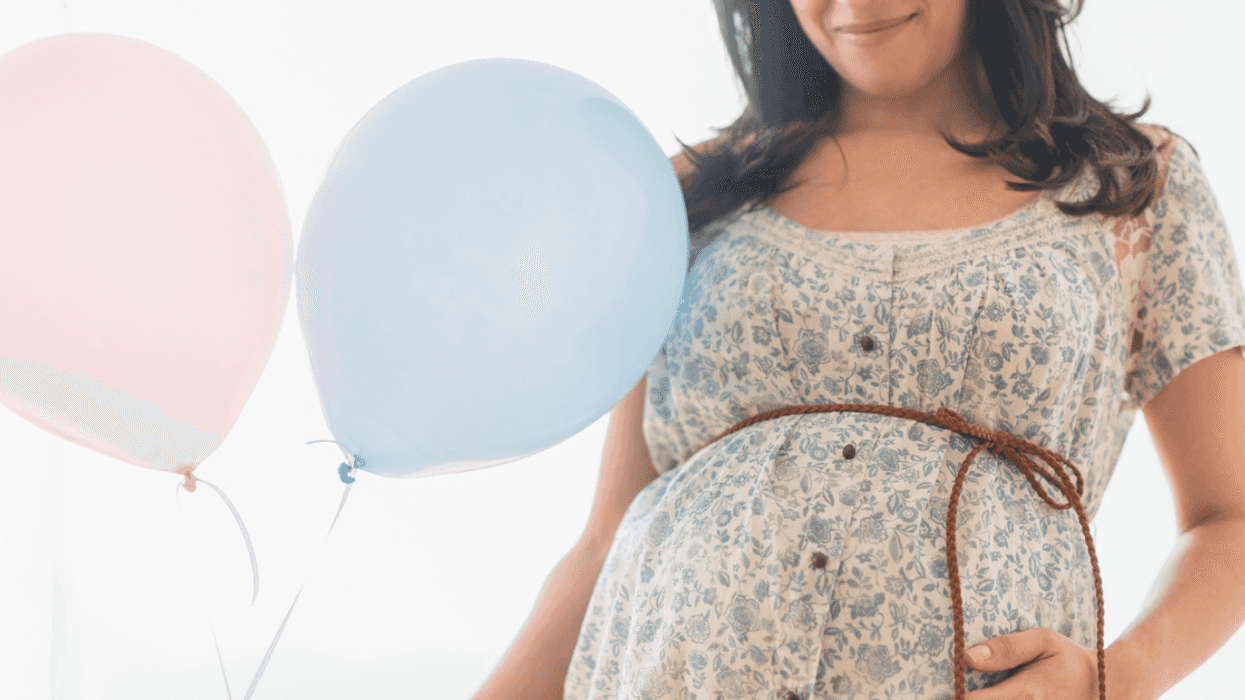 pregnant person holding pink and blue balloons