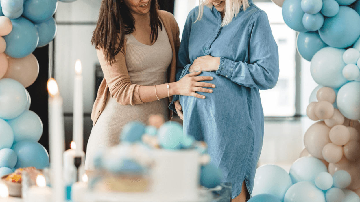 pregnant person standing in blue balloon arch with another person