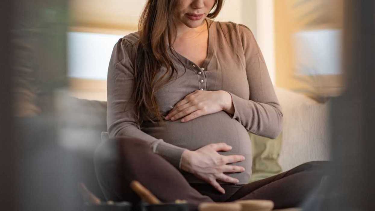 Pregnant woman feeling pain while sitting in a living room.