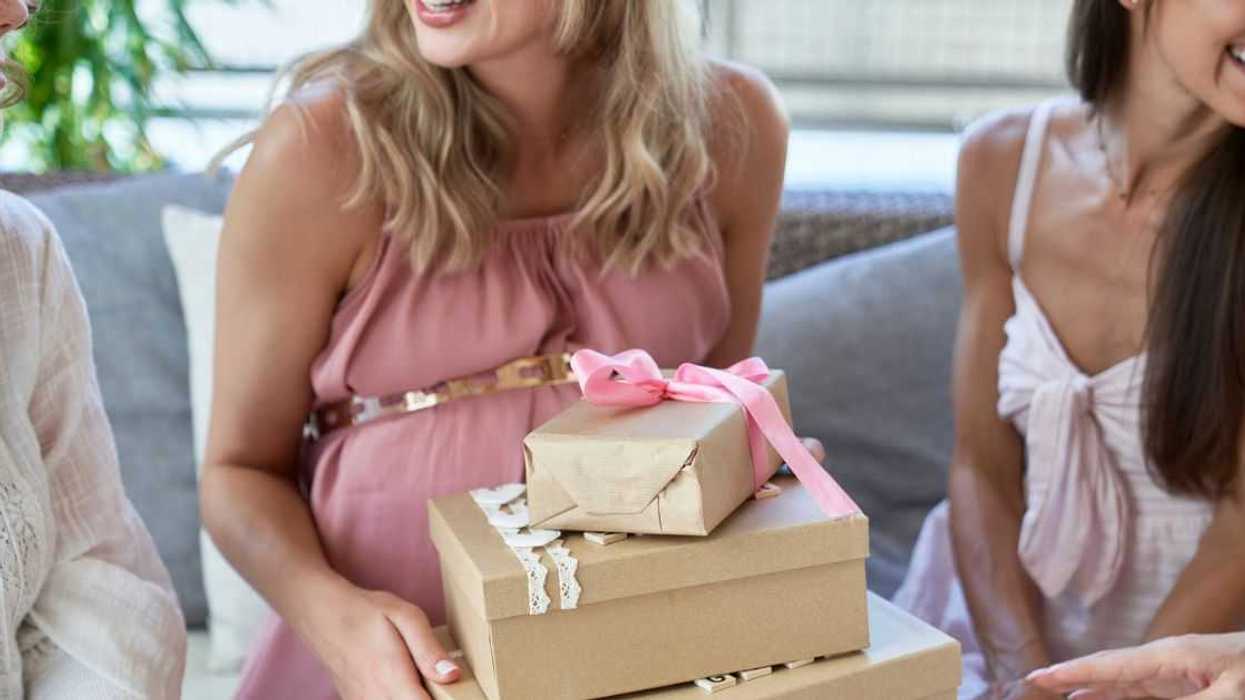 Pregnant woman holding gift boxes by friends at baby shower.