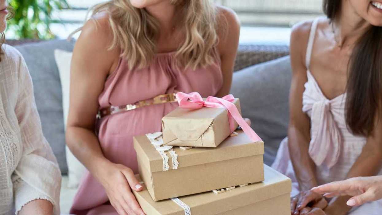 Pregnant woman holding gift boxes by friends at baby shower.