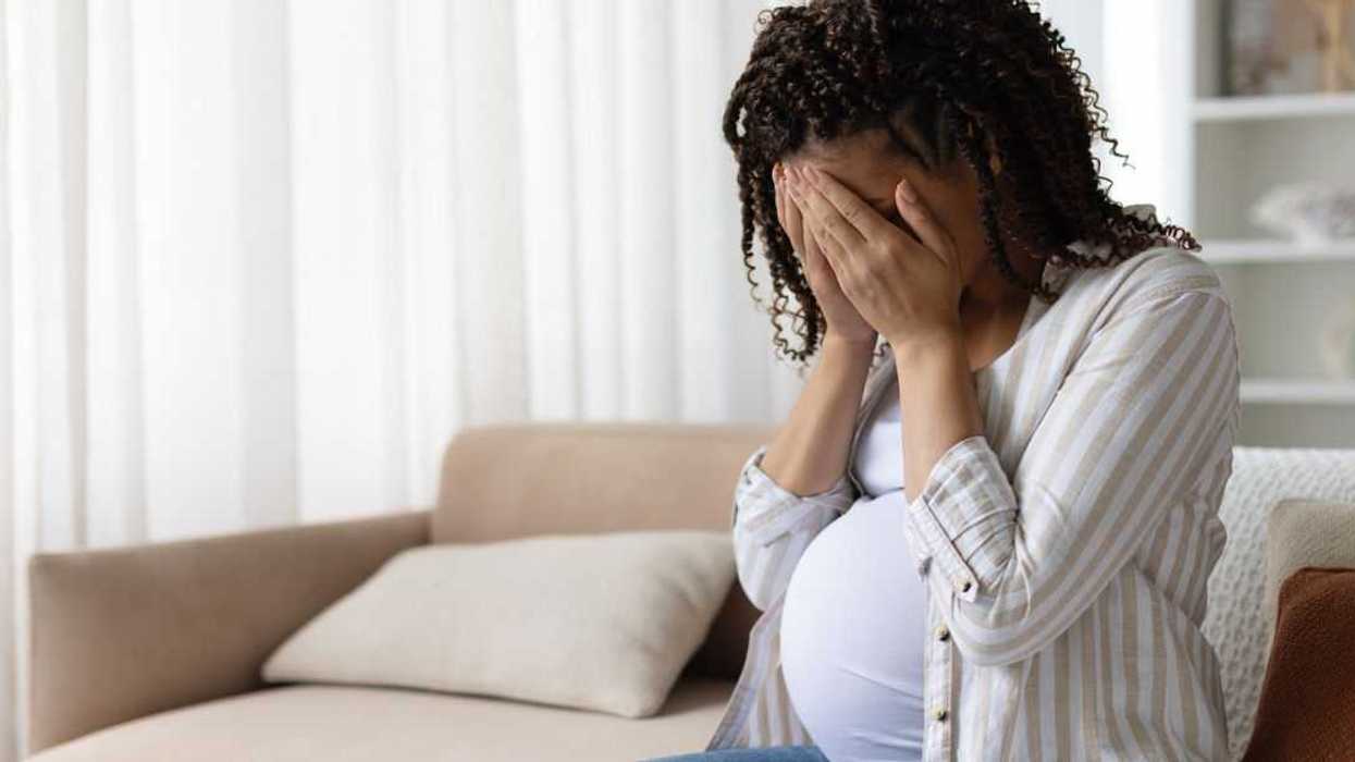 Pregnant woman sitting on a sofa at home with her face in her hands, stressed and upset, concept of anxiety, depression or emotional struggle in maternity.