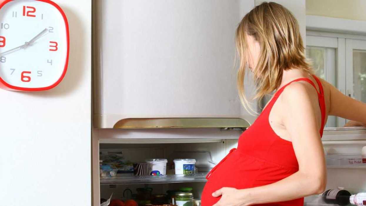 Pregnant woman with cravings looks in fridge.