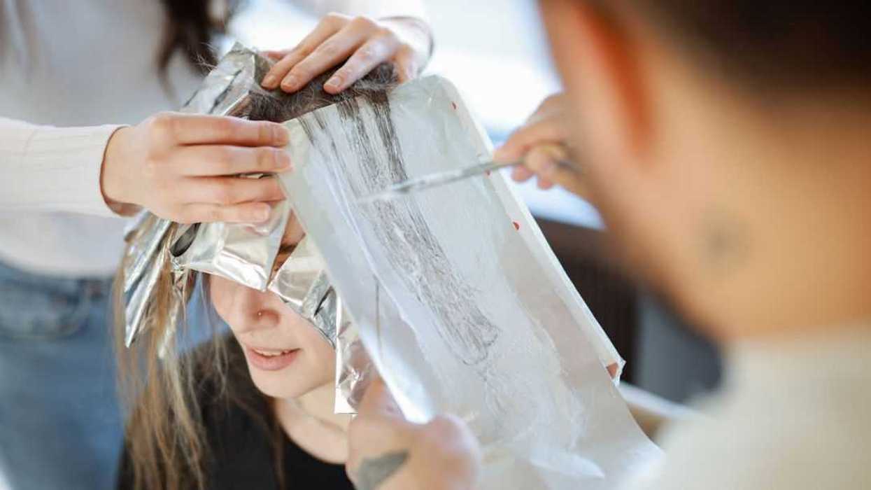 Professional colorist creating a new look on a client. Attractive blonde hairdresser thoroughly dyeing hair of female client while she is sitting in chair in beauty salon.