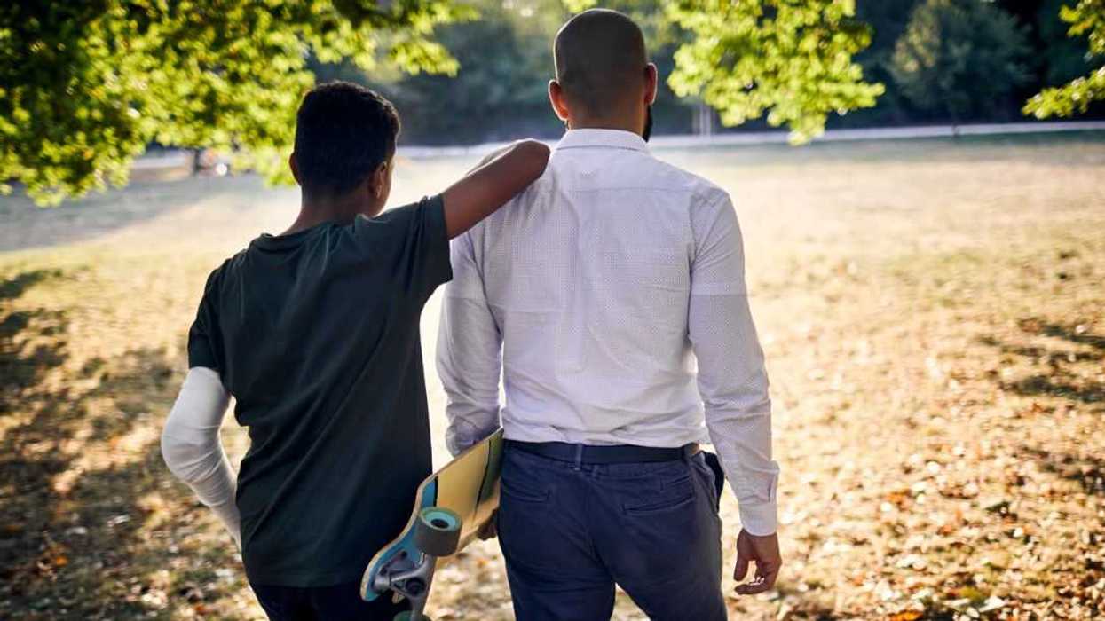 Rear view of a father and son with skateboard walking in a park.