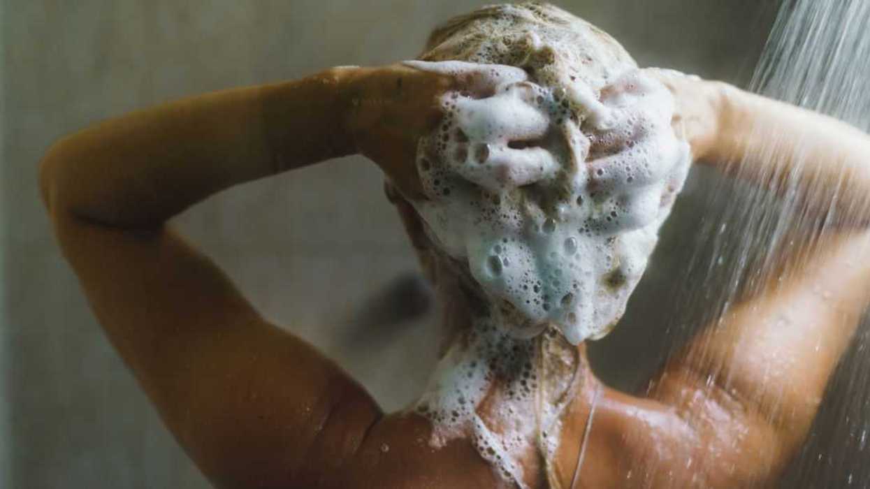 Rear view of a woman washing her hair with shampoo in the shower.