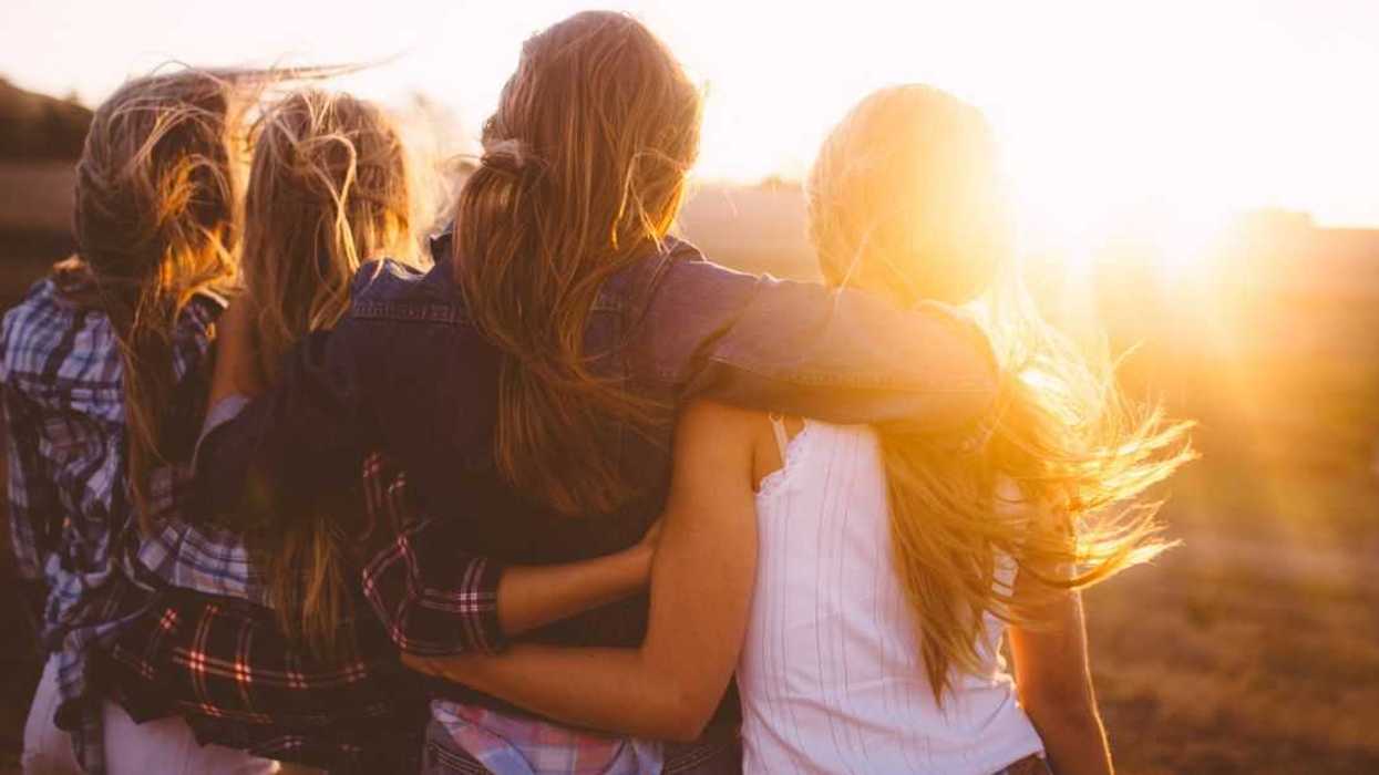 Rearview shot of 4 girl friends looking at the sunset together on a golden summer evening.