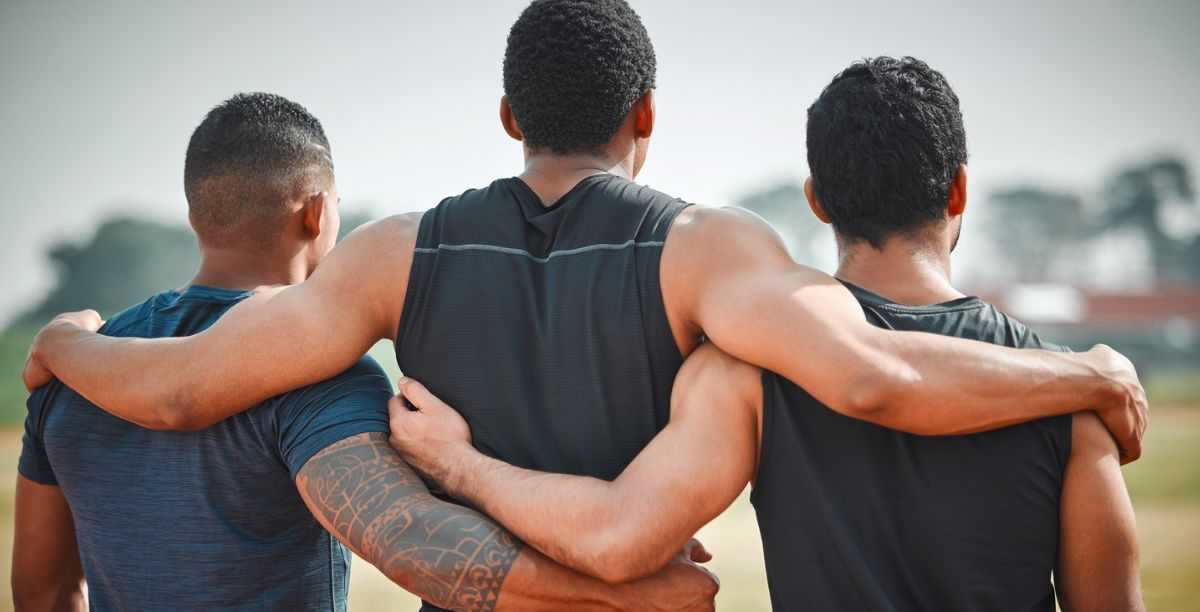 Rearview shot of three unrecognizable young male athletes standing together on an outdoor running track.