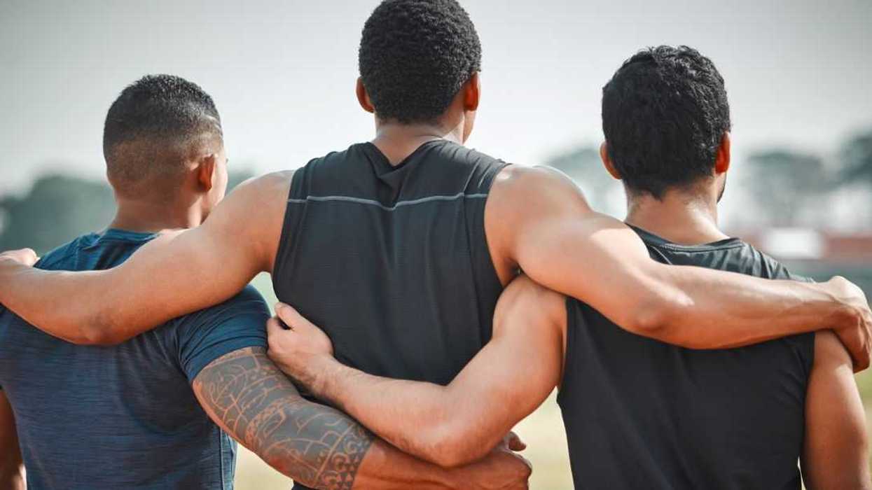 Rearview shot of three unrecognizable young male athletes standing together on an outdoor running track.