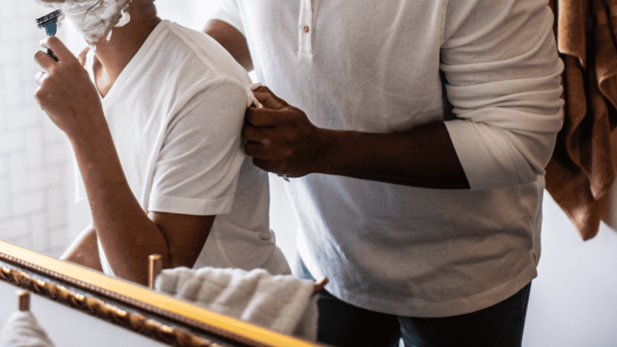 Reflection of a young boy shaving with a man standing behind him.