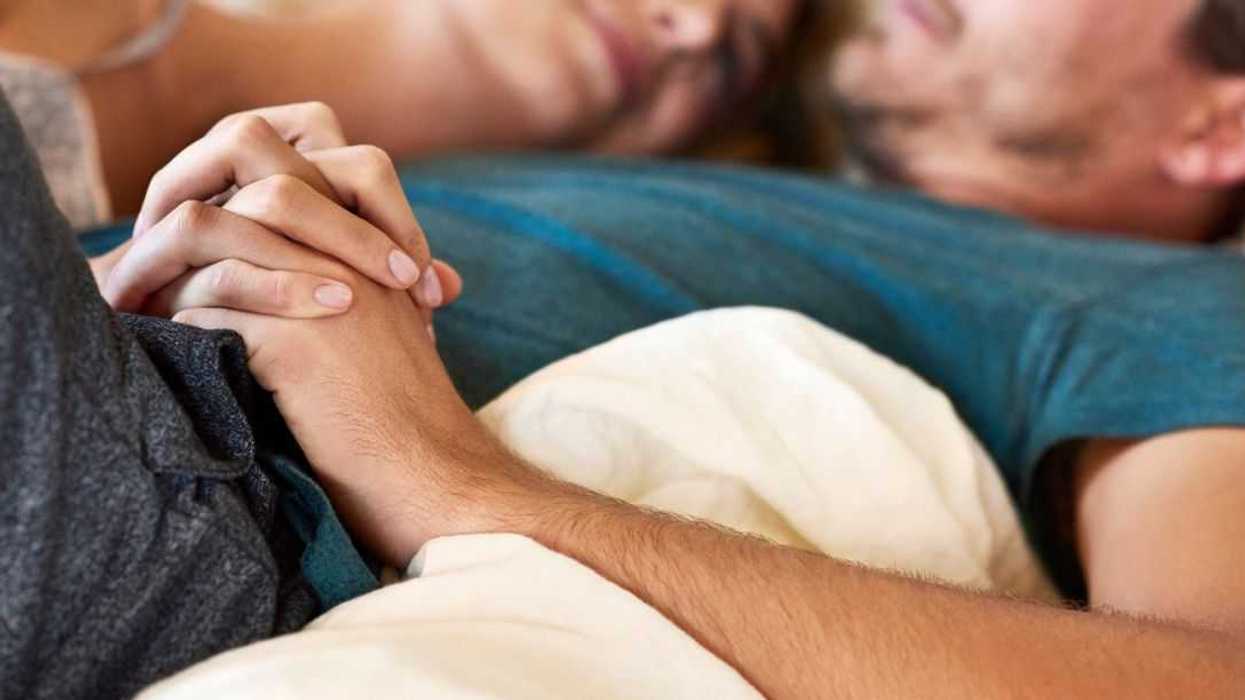 Romantic young couple holding hands in bed. Loving male and female partners spending quality time together. Focus is on their hands.