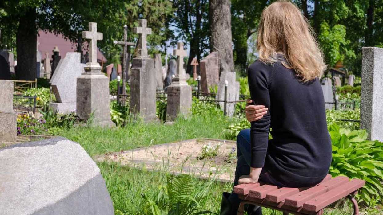 Sad woman sitting near her father's tombstone in cemetery.