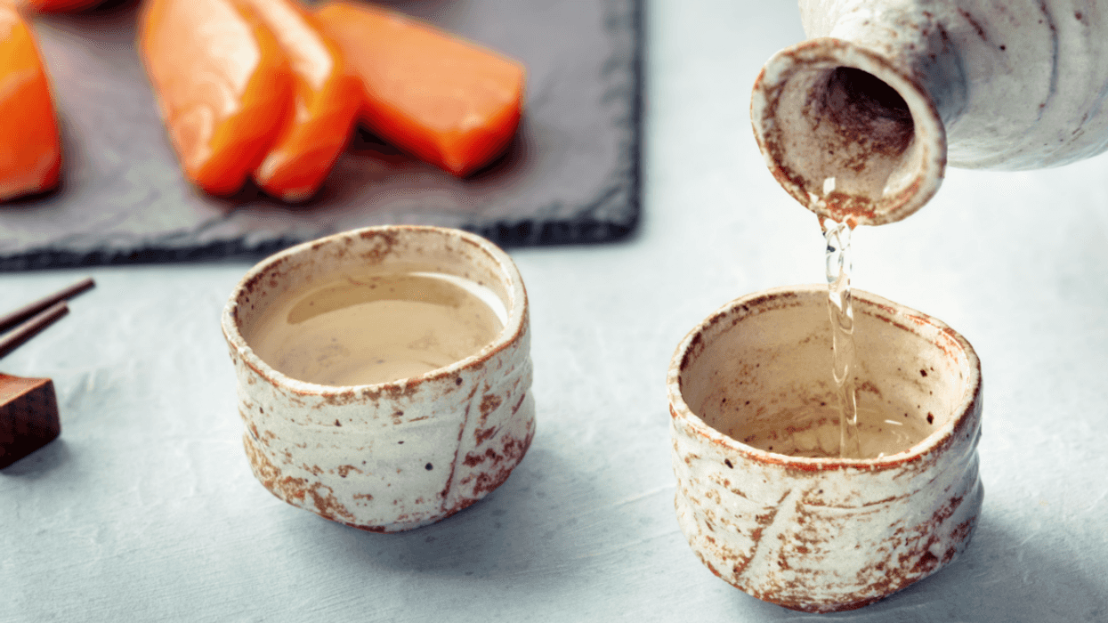 sake being poured into traditional ochoko with salmon in the background
