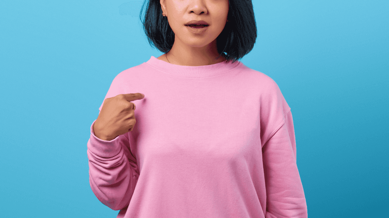 shocked woman in pink top pointing to herself