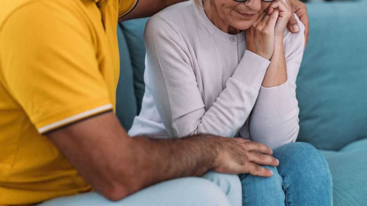 Shot of a mature husband expressing empathy and compassion to his sad frustrated wife. They sit huddled on their couch at home.