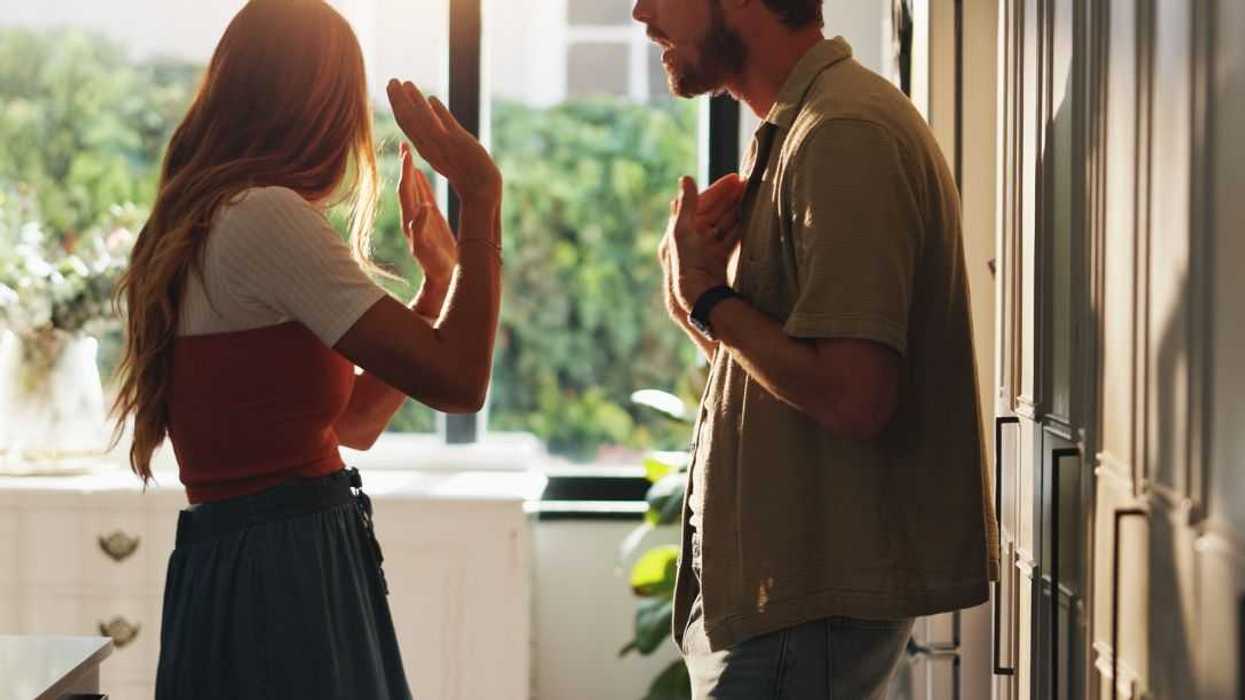 Shot of a young couple arguing in the kitchen. Woman has her head turned away and arms up defensively.