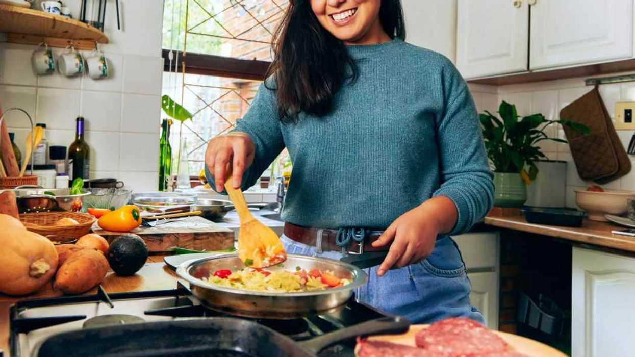 Shot of a young woman stirring vegetables on the stove.