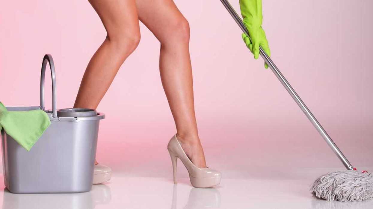 Shot of the legs of a woman in high heels. She is mopping a floor. There is a pink backdrop.