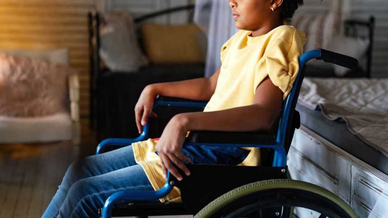 Side portrait of disabled little girl sitting in a wheelchair at home.