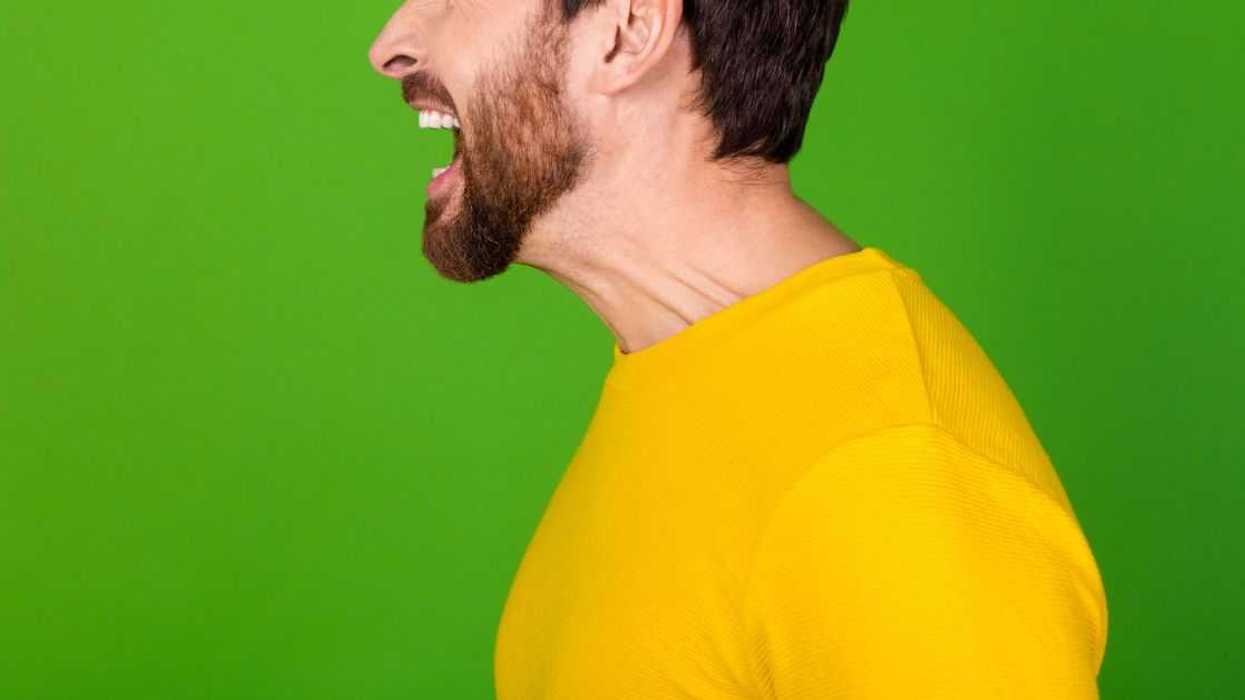 Side profile photo of an angry man with a beard, dressed in a yellow shirt. He is loudly screaming into an empty space, he isolated on a vibrant green color background.