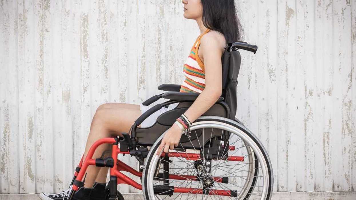 Side view of a disabled teenage woman in a wheelchair outdoors.