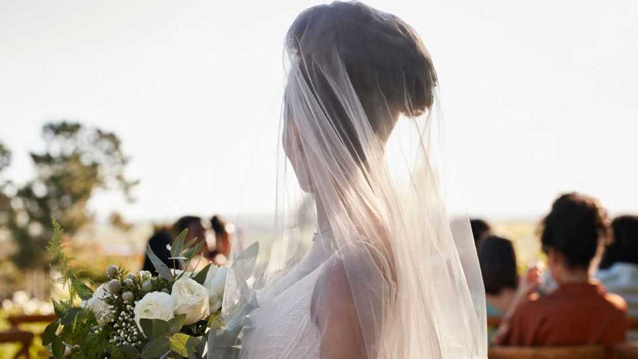 Side view of a young bride wearing a veil, standing with a flower bouquet at a wedding ceremony.