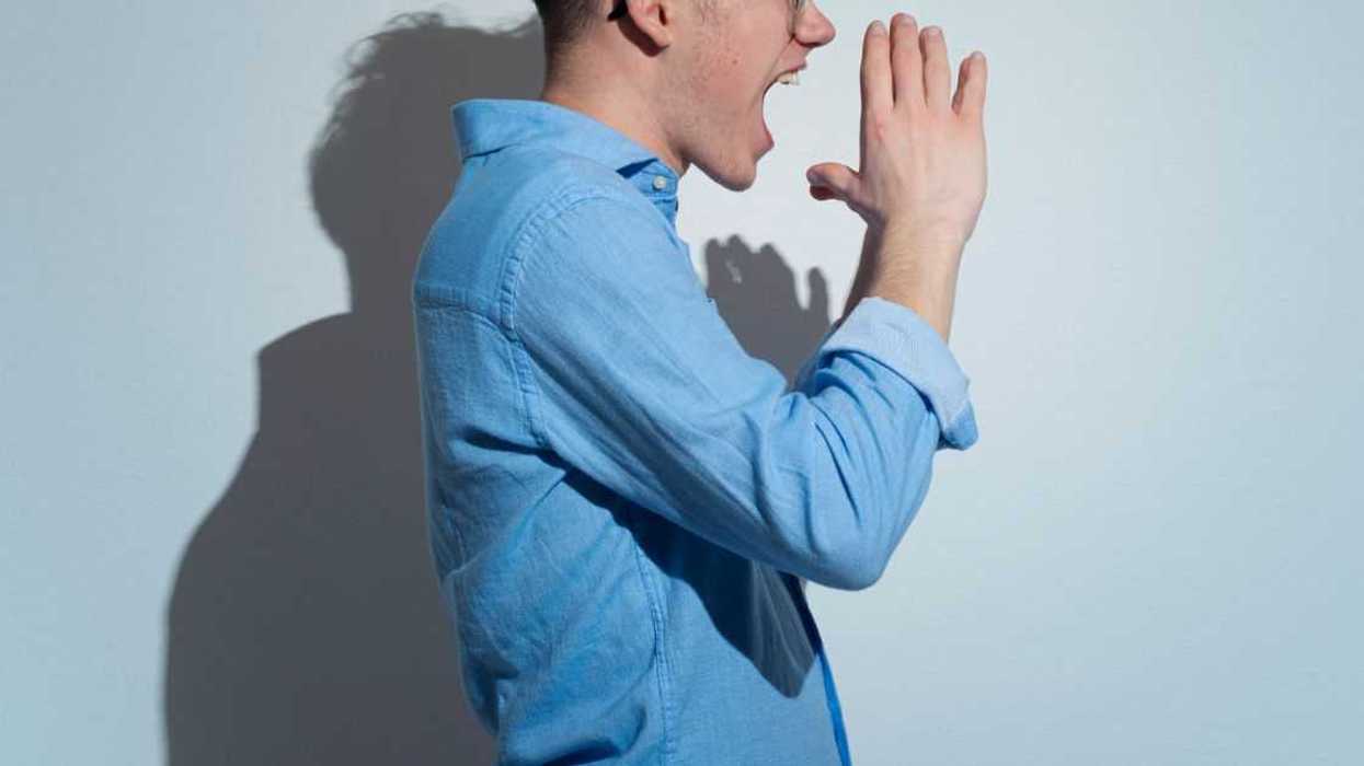 Side View of angry man screaming while standing against Light blue background.Studio shot.