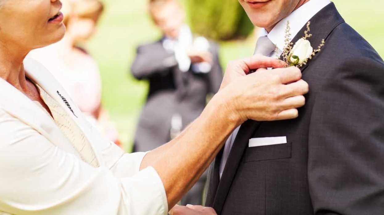 Side view of mother pinning boutonniere on groom's suit at garden wedding.