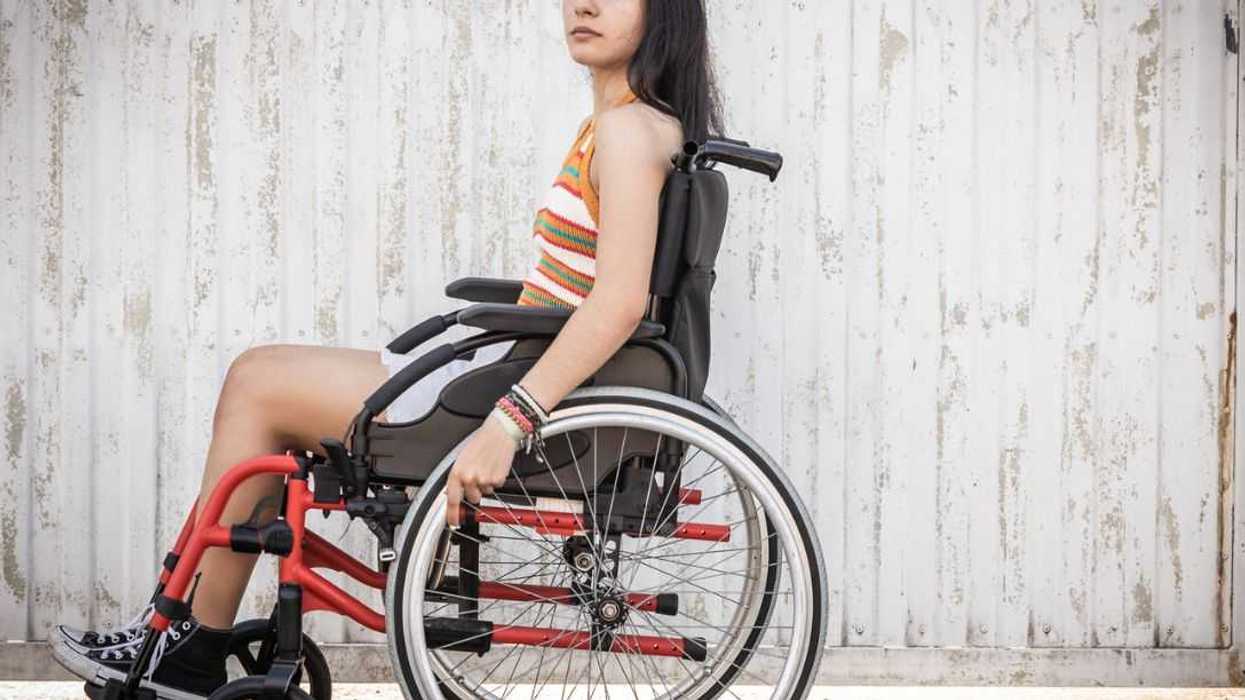 Side view of young woman in a wheelchair looking directly into camera with sad look. Young woman living with a disability.