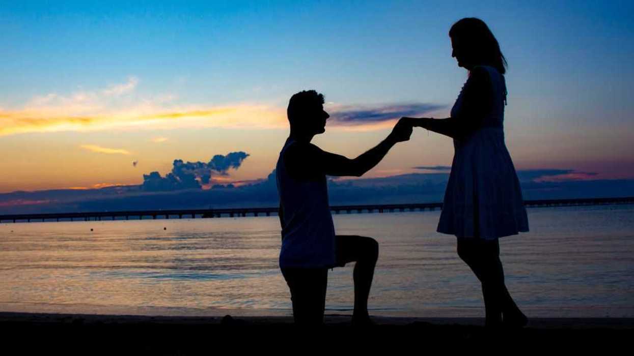 Silhouette of a man proposing to a woman standing on the beach against the sky during sunset.