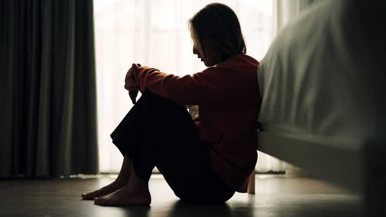 Silhouette of a woman, sad and depressed, sitting on the bedroom floor.