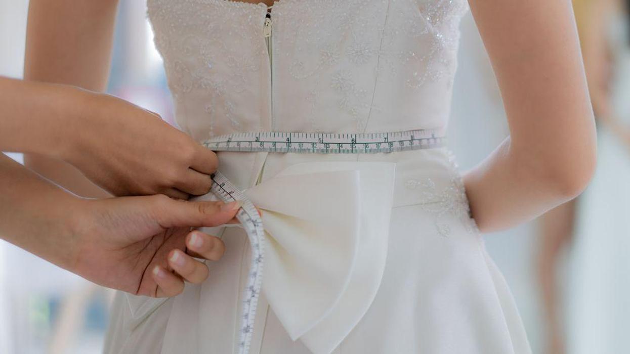 Skillful dress designer fitting wedding gown to woman in her boutique. Woman making adjustments to bridal gown in fashion designer studio.
