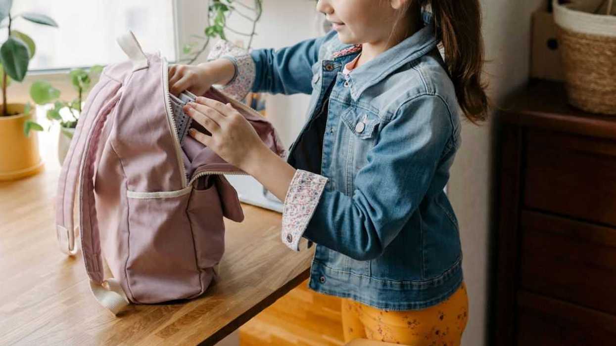 Smiling girl opening backpack on table at home.