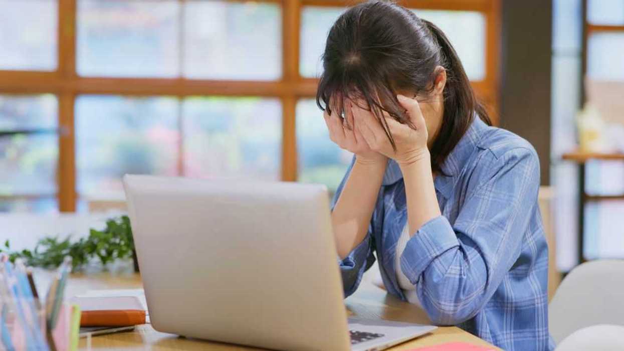 Stressed woman sitting in office is upset, she has her face in her hands.
