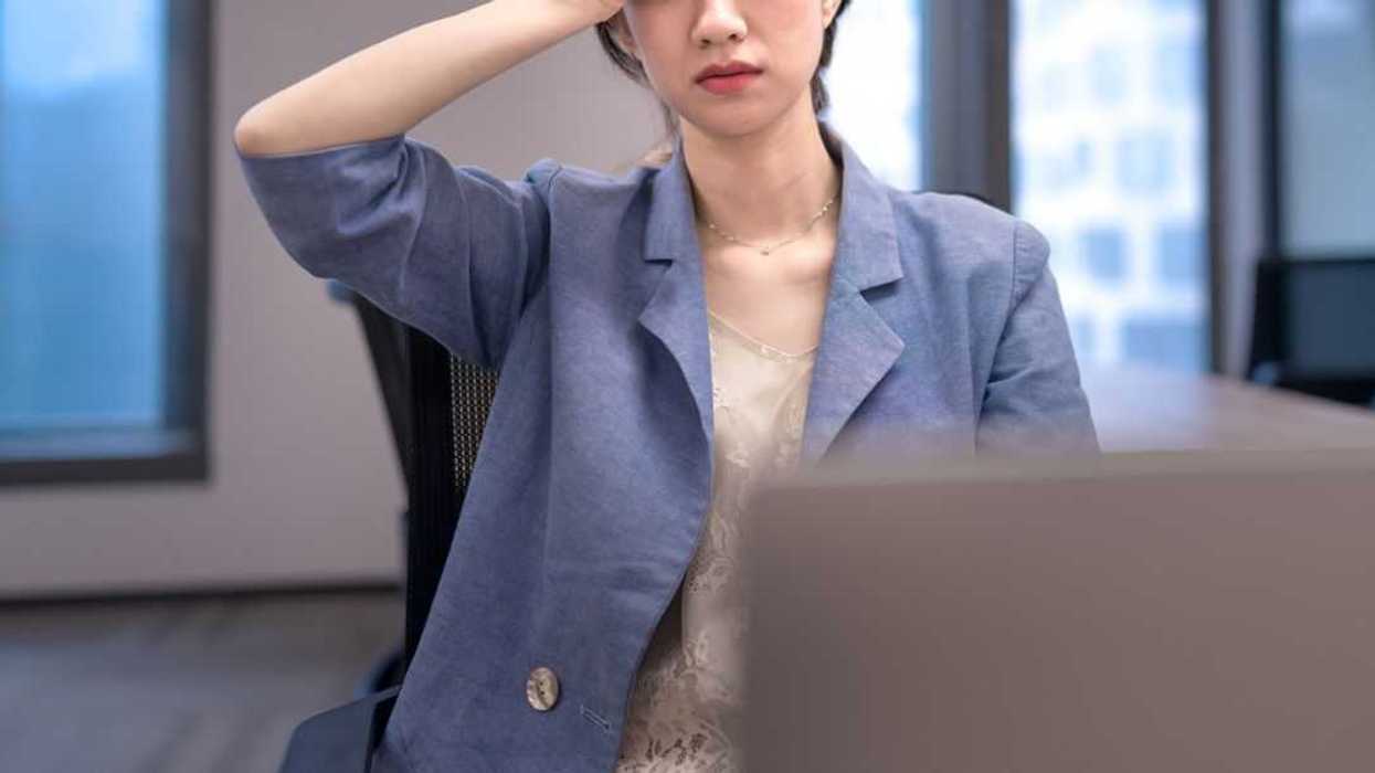 Stressed young businesswoman in the office, holding her hand to her head.