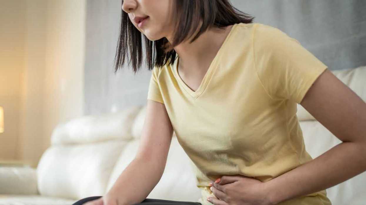 Stressed young woman sits on a sofa at home having a stomach ache or period. Menstrual gynecological concept.