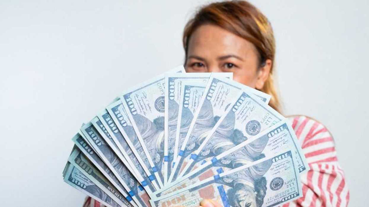 Studio shot of a woman holding up a fan of money.