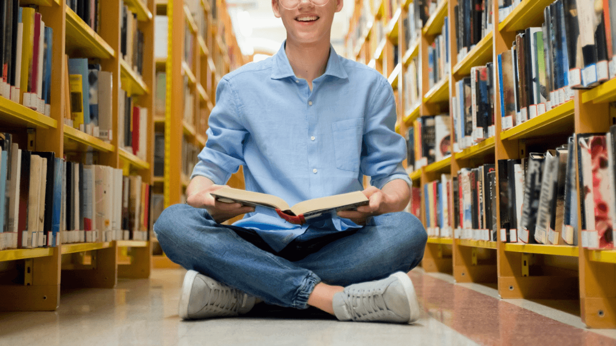 teen boy sitting on library floor looking at a book