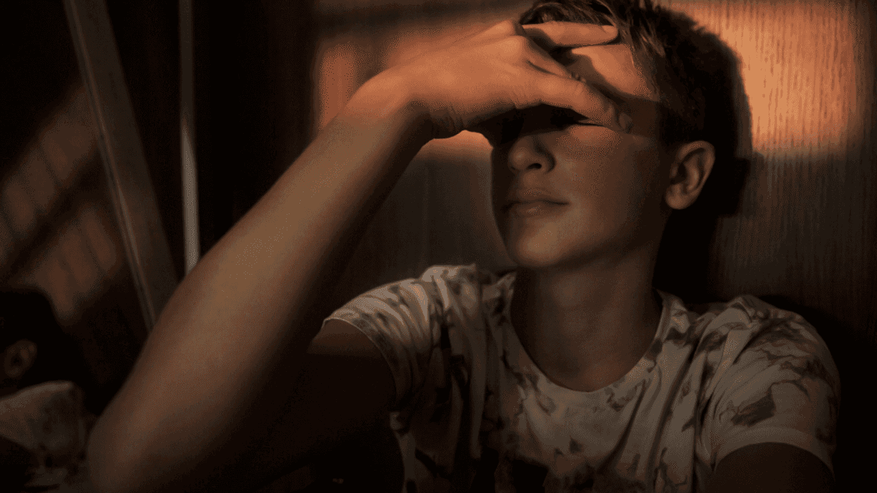 Teenage boy leaning against the wall with his head in his hands.