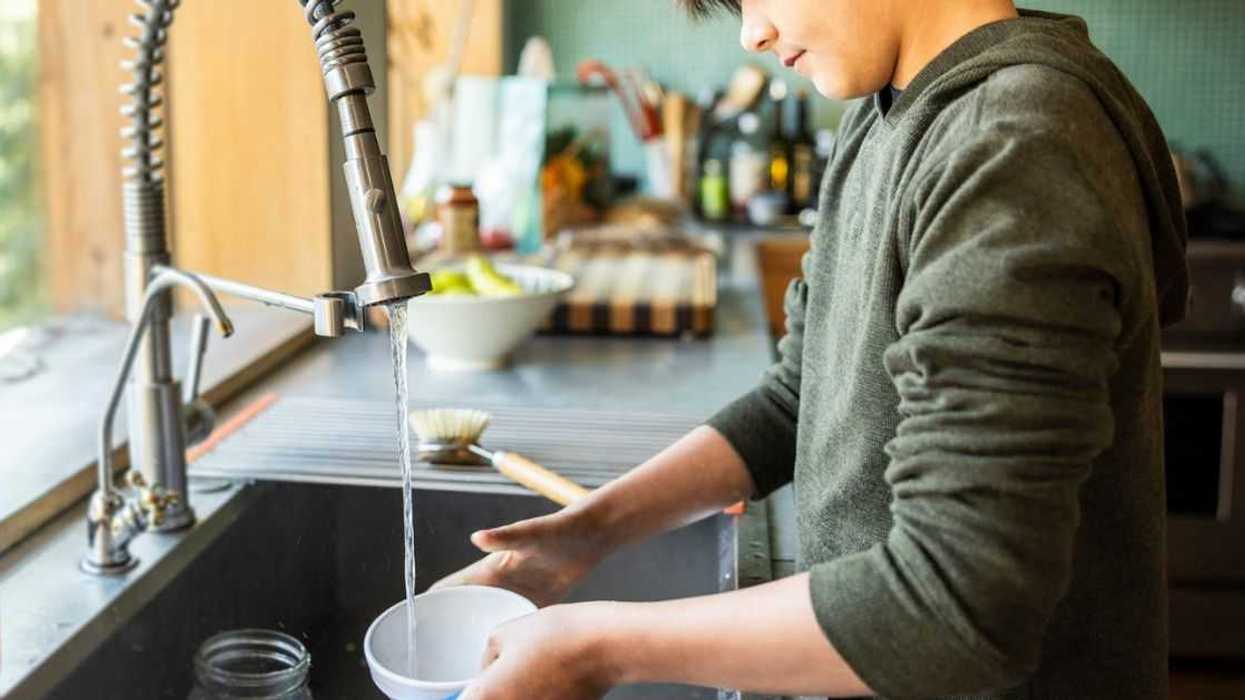 Teenage boy washing dishes in kitchen.