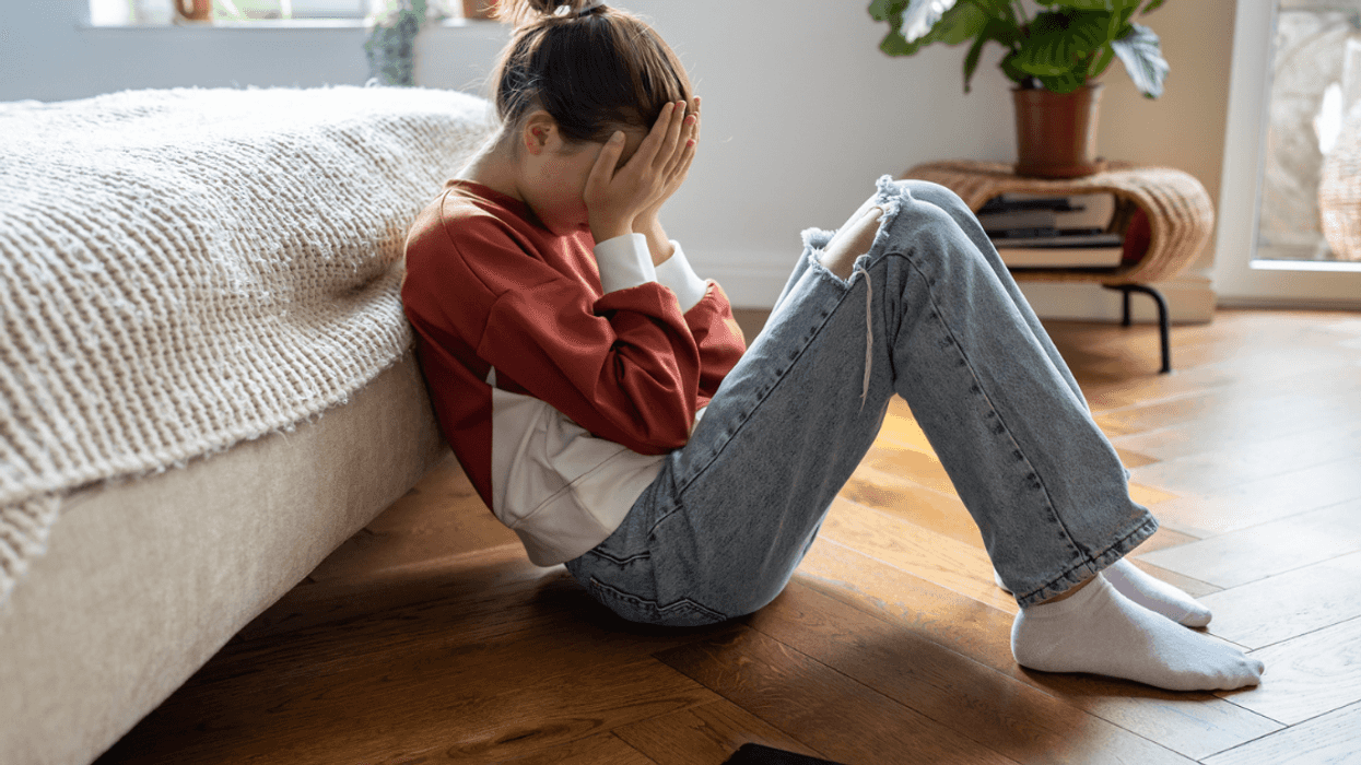 Teenage girl lying against her bed with her head in her hands.