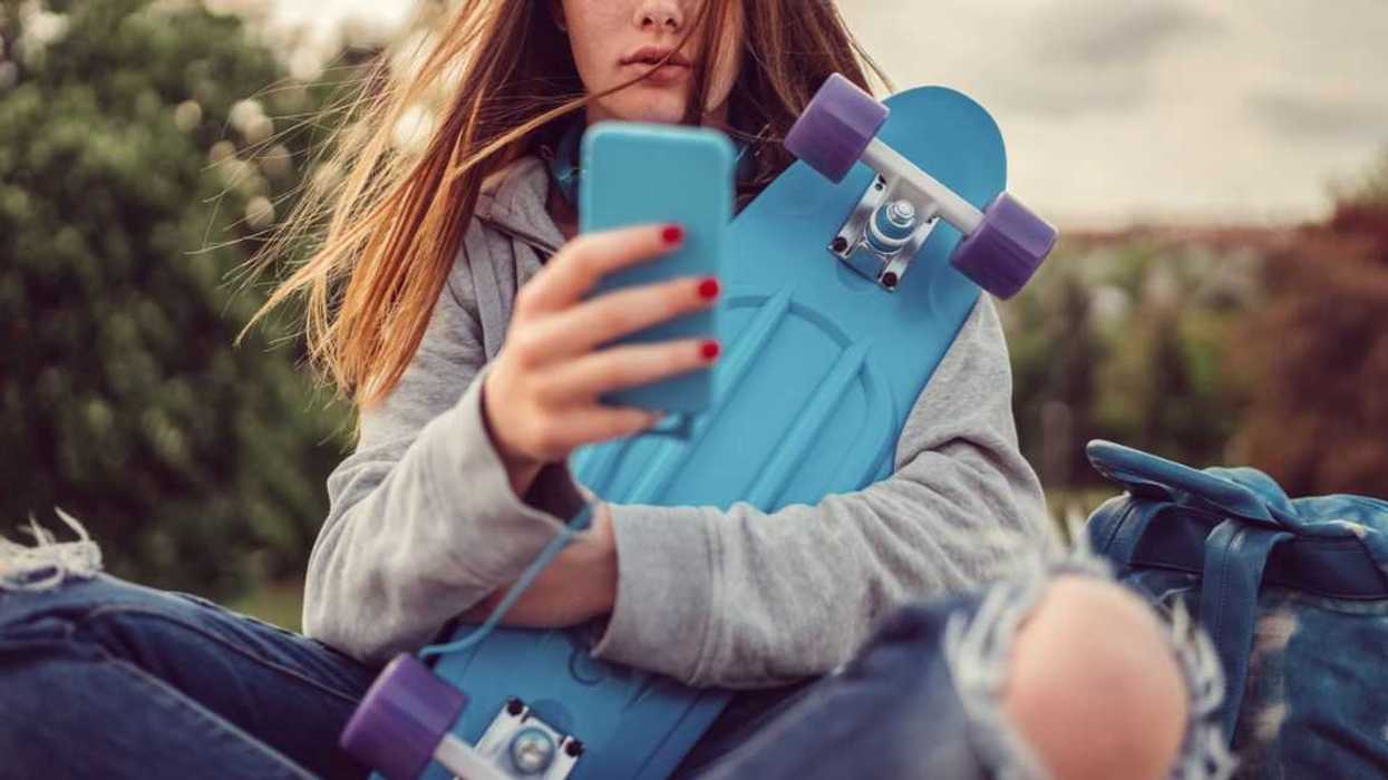 Teenage girl with skateboard texting on smartphone.